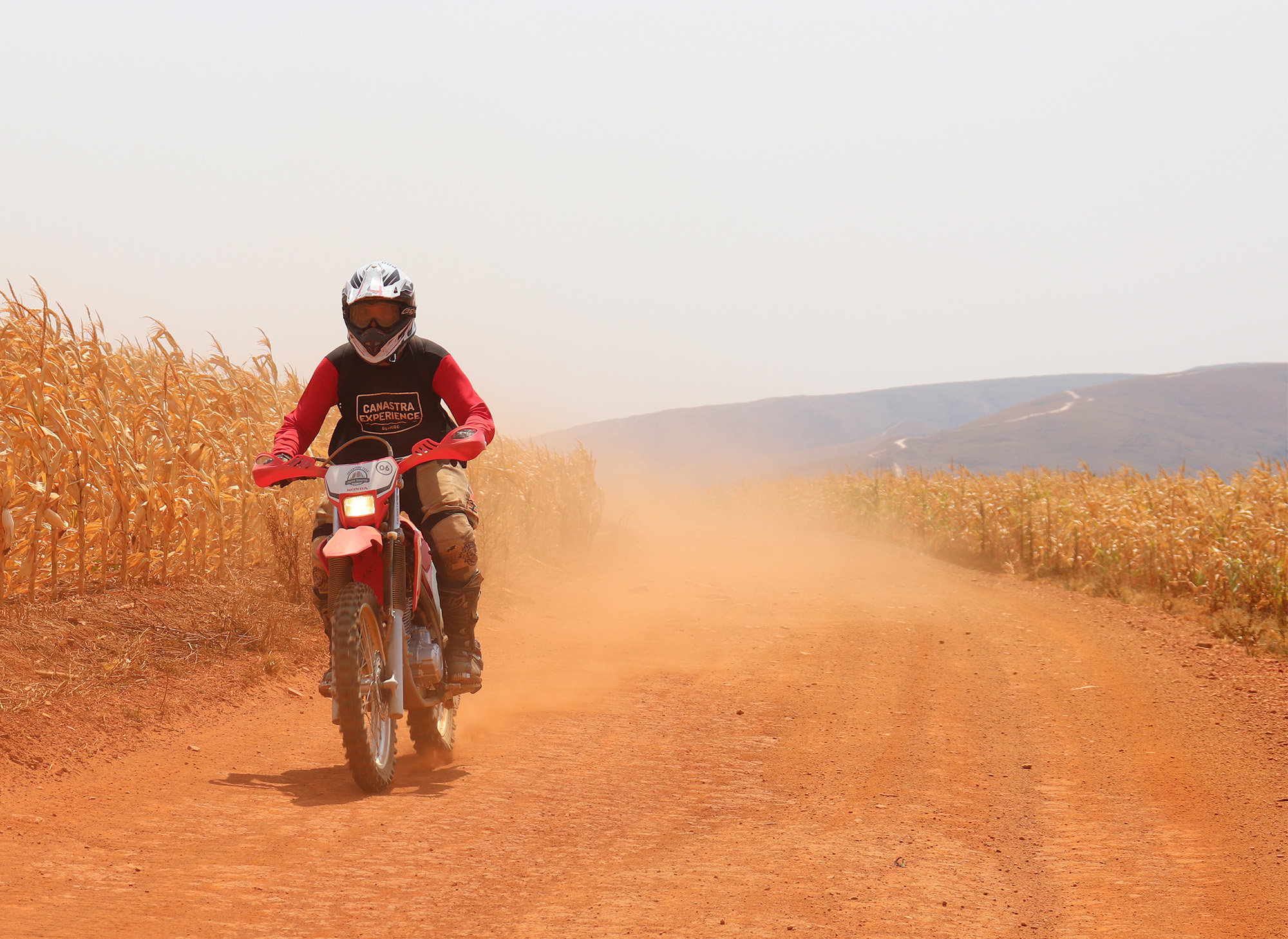 Piloto em moto de trilha por estrada de terra, em fotografia de referência